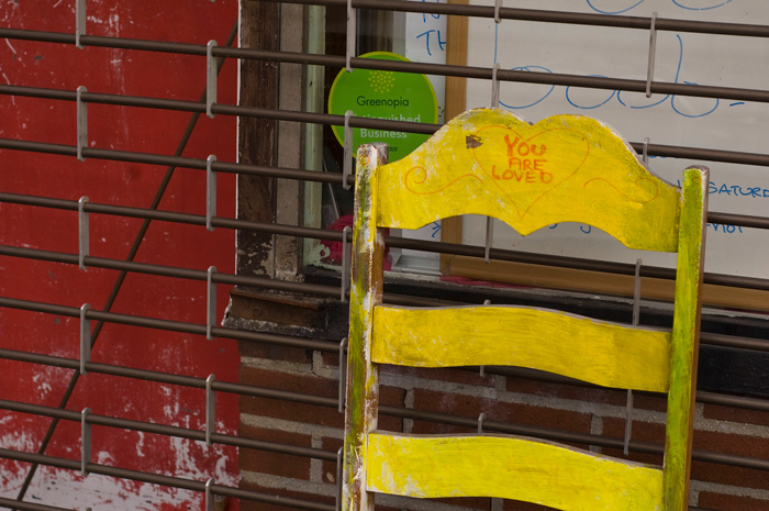 The words 'You Are Loved' have been hand-painted on the back of a colorful wooden chair.