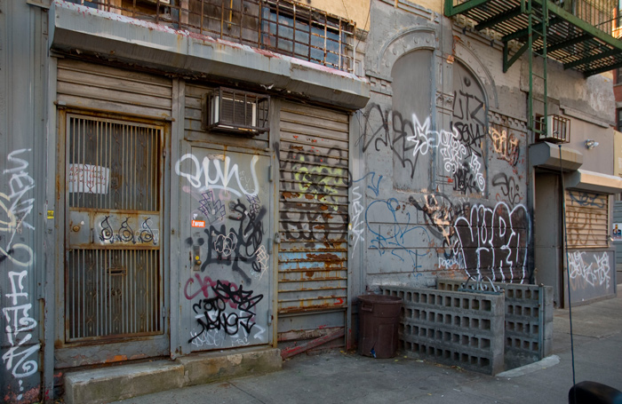 Graffiti has covered a grey block composed of doors and rolled down storefronts.