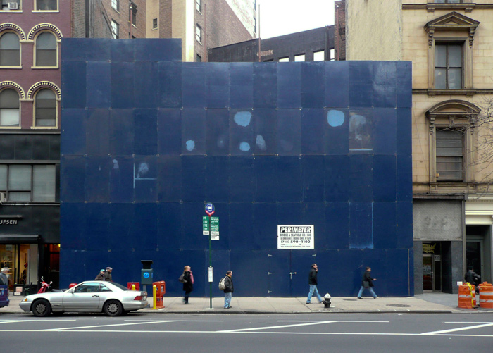 Plywood, painted blue, covers an old building undergoing renovations.