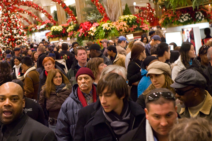 A department store, decked in holiday colors, is packed with shoppers.