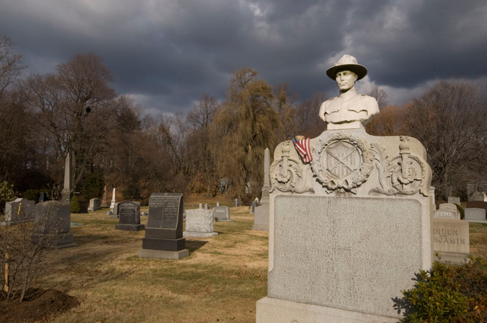 A tombstone is capped with a soldier's bust, and it stands out among shorter stones in a cemetery.