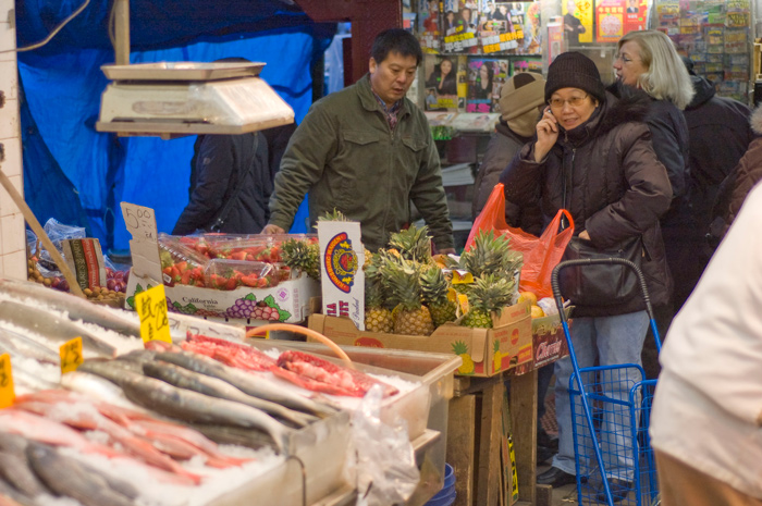 A shopper pauses to talk on her cell phone while standing in front of a fish stall.