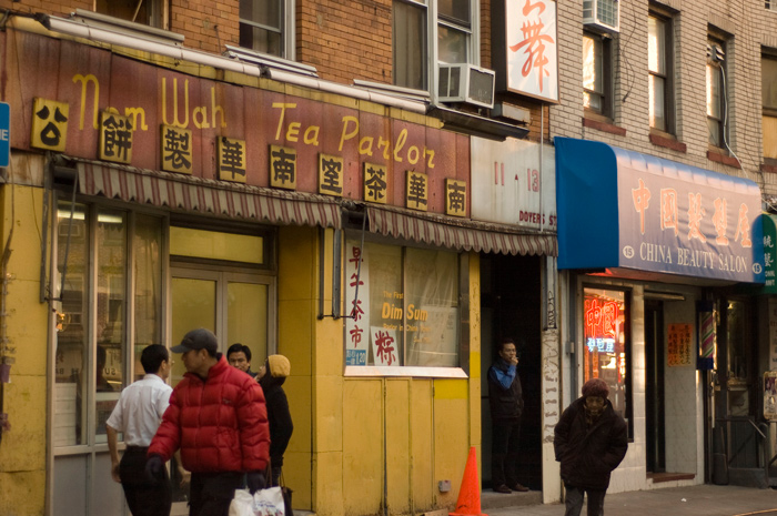 A man smokes a cigarette in a doorway while pedestrians pass.