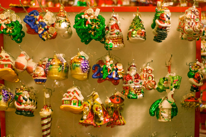 Colorful Christmas ornments of molded glass hang on strings from pegs in a store display.