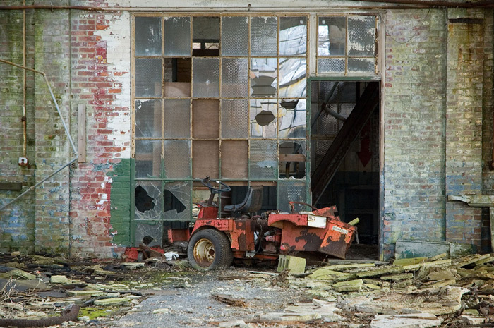 A dilapidated, rusting motor cart is parked in front of broken window panes, and surrounded by debris.