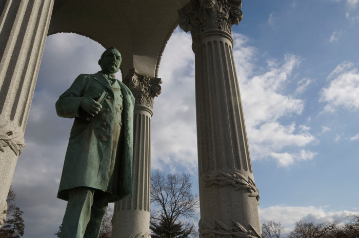 A statue of a man, holding a book, stands under a rotunda.