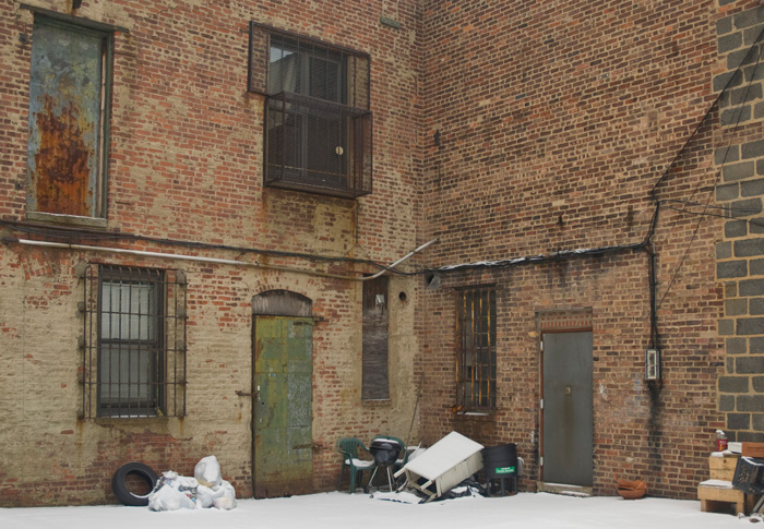 The backs of two brick buildings come to a right angle, and their metal doors looks very old.
