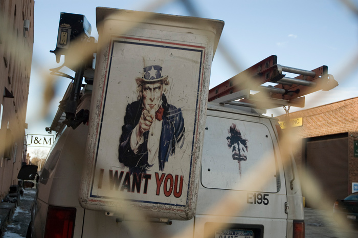 A cherry picker behind a fence has the old Uncle Sam 'I Want You' poster glued on its side.