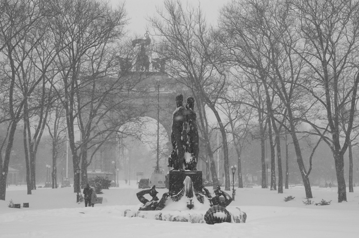 A statue group stands erect, with an arch in the distance, while heavy snow falls.