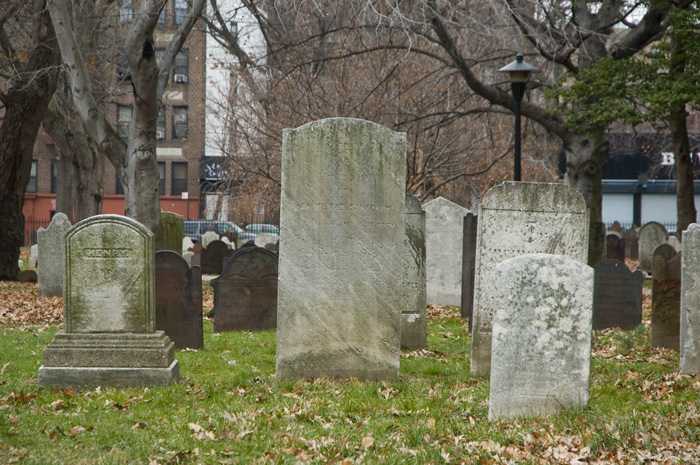 Several old tombstones stand upright in a church yard where the city has built around it.