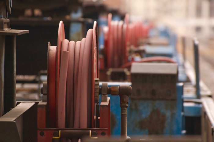 On each of a series of flatbed rail road cars is a red spool with a red rubber hose.