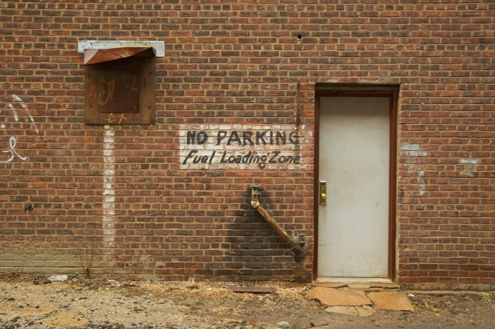 A sign warns people not to park in the fuel loading zone, where a pipe on the old brick wall shows signs of oil drippings.