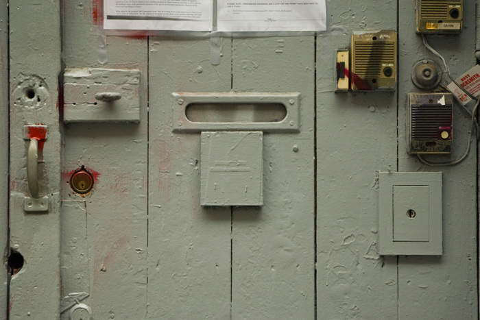 A wooden door has all sorts of buzzers, locks, and hasps on it.