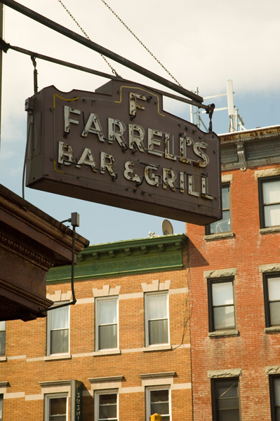 A hanging neon sign stands out against tan brick buildings in the background.