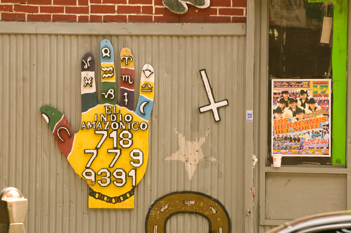 A multi-colored hand shows the phone number of the botanica store, but an upside-down cross reveals the store is closed.