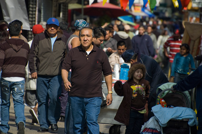 A sidewalk is filled with pedestrians of Hispanic background, hurrying along their way.