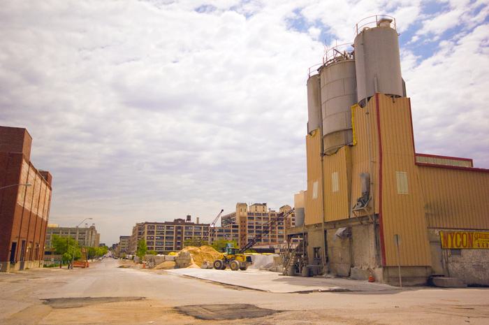 The towers of a cement factory stands at the beginning of an empty industrial street.