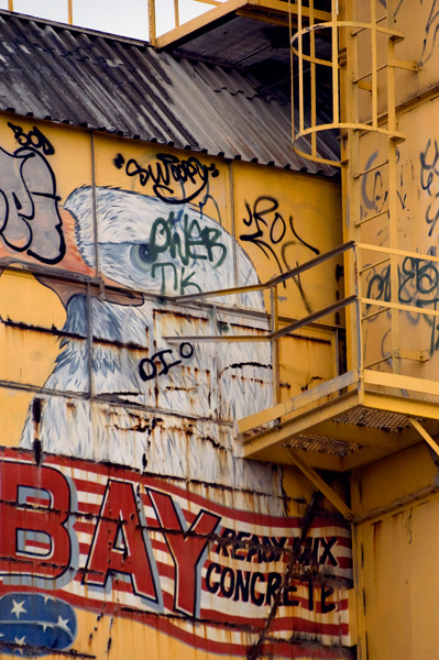 A yellow cement factory has a bald eagle and an American flag painted on its side.