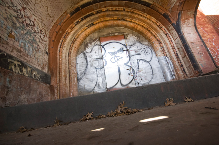 Boarded-up doors below brick arches have been covered with graffiti.
