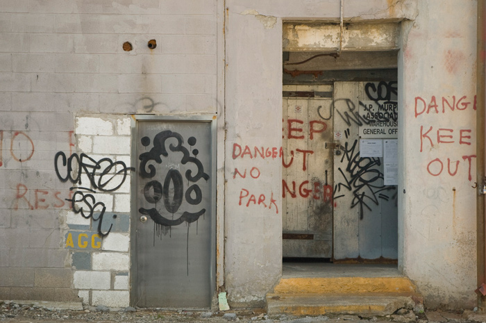 A darkened entryway has been spray-painted with crude warning messages to keep out, danger.