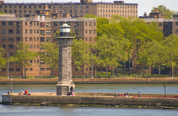 A lighthouse stands on the tip of an island, while people relax around its base.