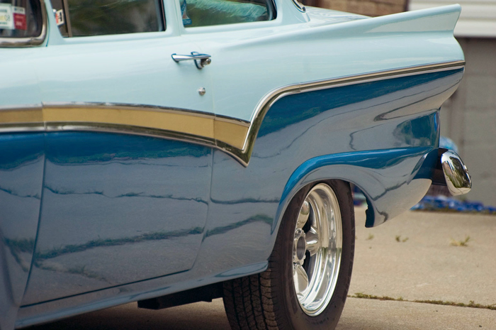 A blue and aqua car from the fifties, nicely waxed, sits in a driveway.