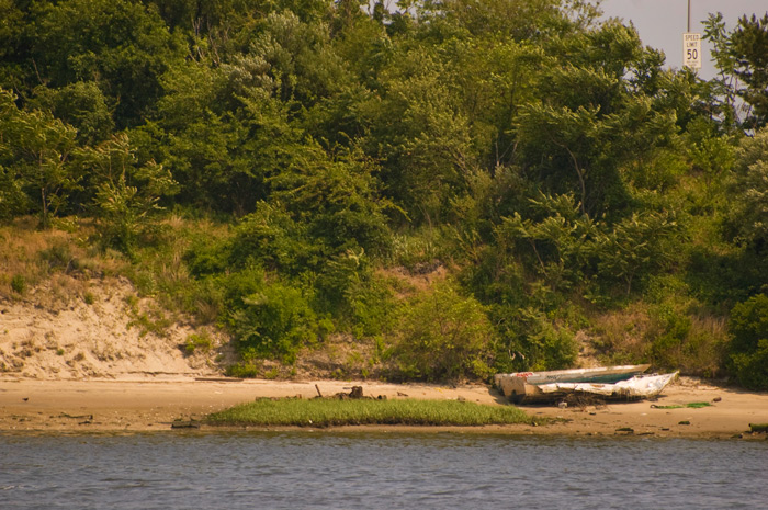 A small, worn out skiff lies on a shoreline, with no signs of attention in years.