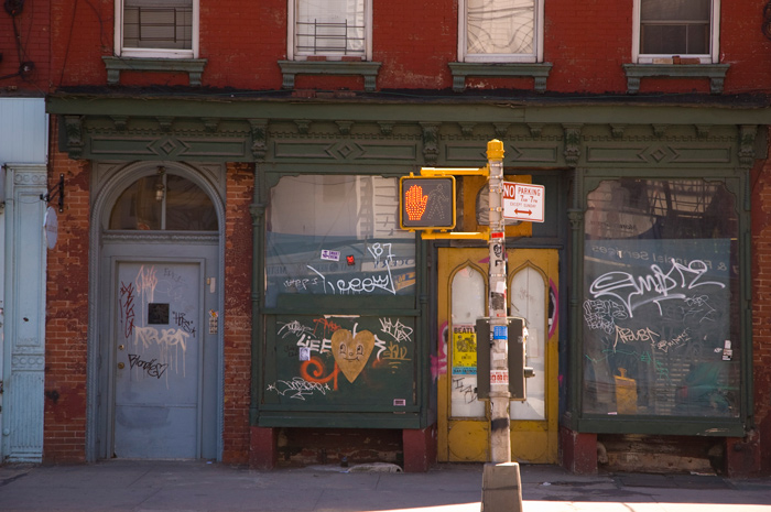 The glass windows and wood panels of an old storefront have been covered with graffiti tags.