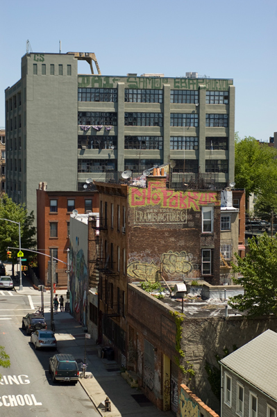 A city street with an old factory, brick buildings, and a cafe with a mural on its side.