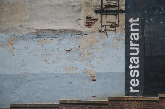 Paint peels on an old wall, completely blank except for the word 'restaurant.'