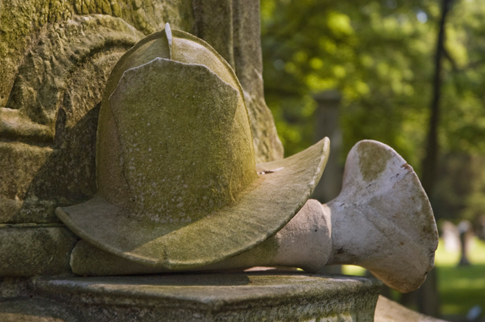 A tombstone is topped with a fire helmet and horn.