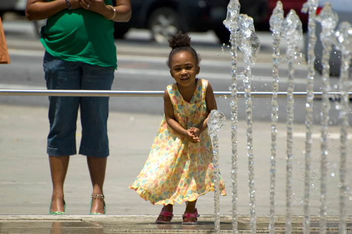 A child smiles at the rhythmic pulses of a water fountain.