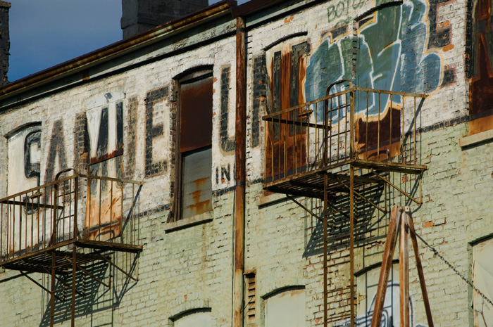 A brick building, in fading green paint, has several layers of graffiti on it.