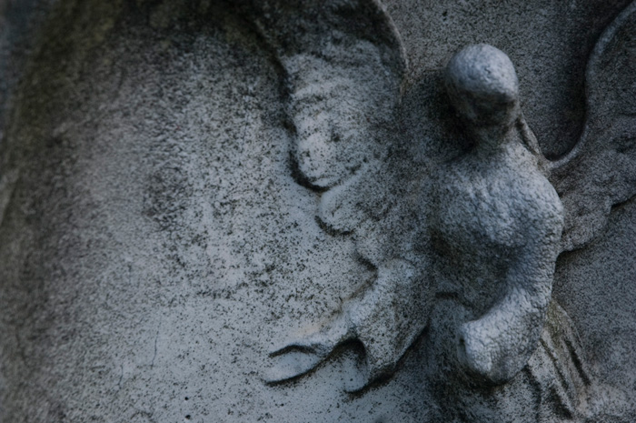 A worn angel in relief, in gentle curves, decorates a tombstone.