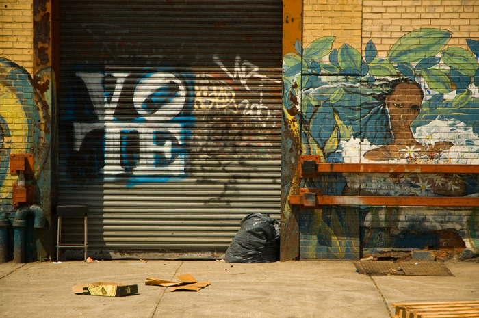 Walls with a tropical mural are on each side of a garage door that's been painted with the word 'Vote.'