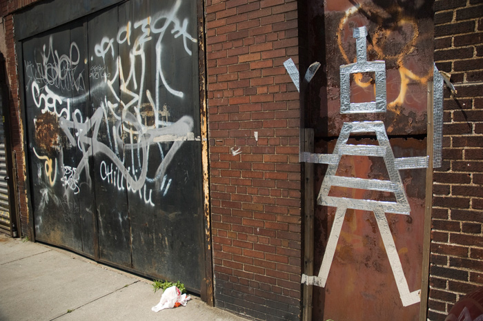 The outline of a robot, made of metallic industrial tape, has been put on an industrial wall.