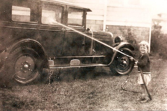 An old photo from the 1920's shows a toddler hosing down a car.