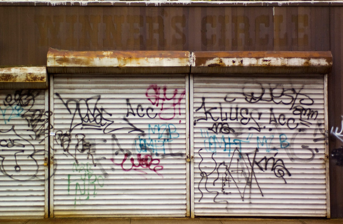 The remnants of sign, reading 'Winners Circle,' are above graffiti-covered roll-down doors.