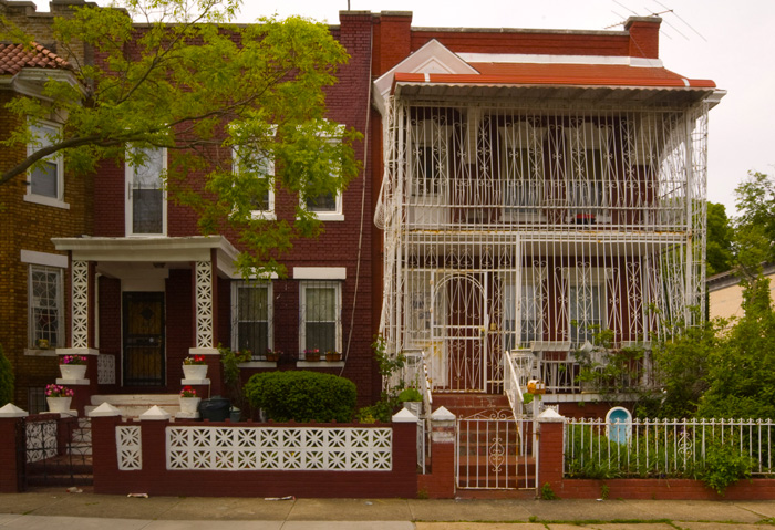 Of a pair of houses, one has steel gates all over its front porch.