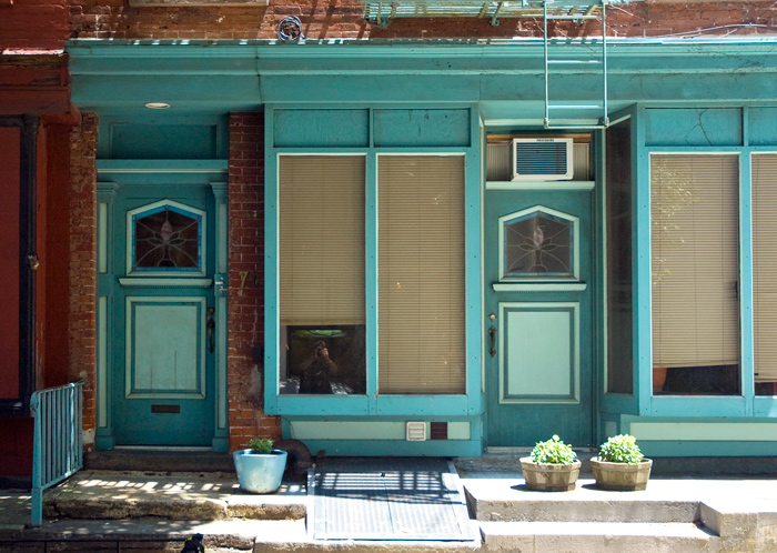 Blinds are pulled down in the windows of old storefronts where people now live.