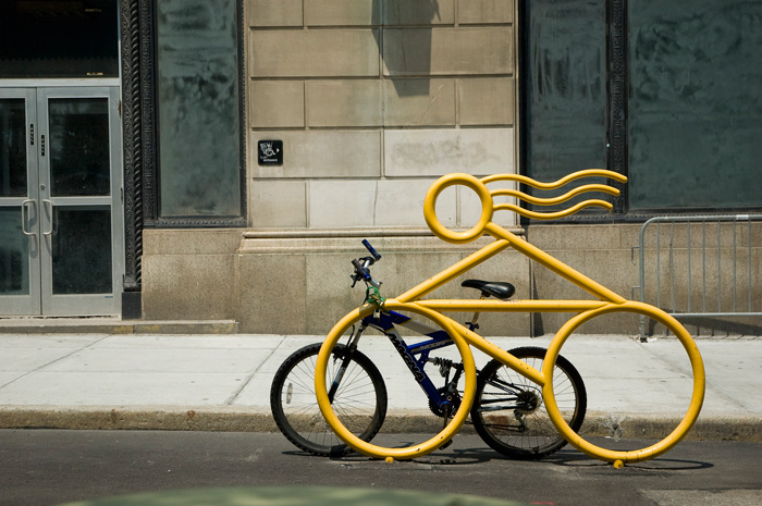 A bike rack on a city street is shaped like a rider on a bike, with long hair flying back.