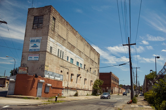 A triangular bulding sits on an empty street, with barbed wire fencing nearby.