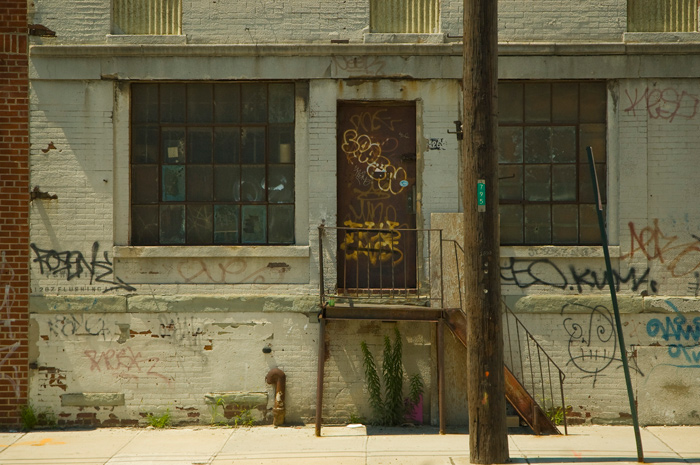 A rusty metal stair leads to a rusty metal door on an old brick building, all covered with graffiti.