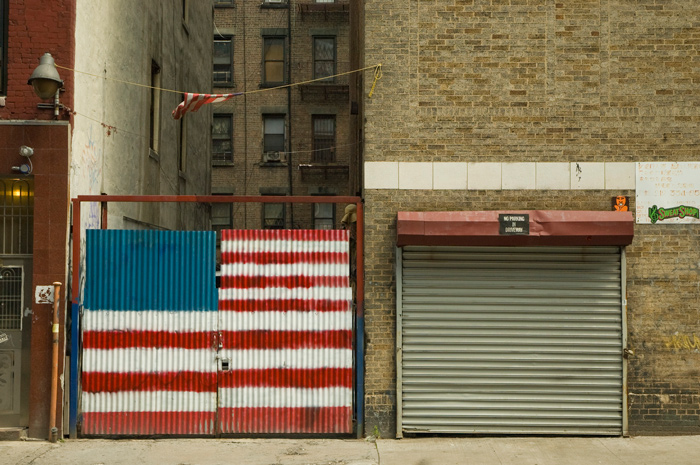 A corrigated steel door in front of an alley has been crudely painted with an American flag mural.