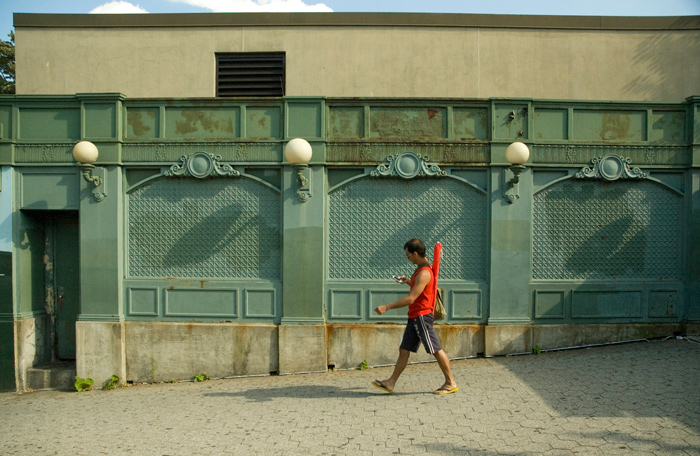 A man wearing red consults his cell phone while passing in front of a green wall.