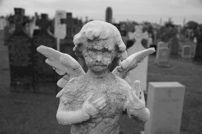 A worn cemetery cherub stands amid several tombstones.