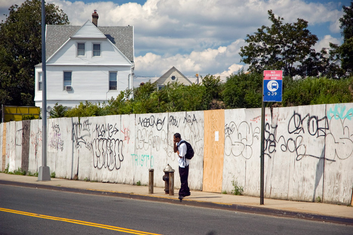 A youth talks on his cell phone, while waiting for a bus on a deserted street.