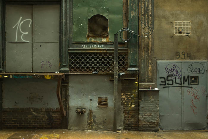 Metal doors, grates, laoding docks, and electrical conduits on one side of an alley.