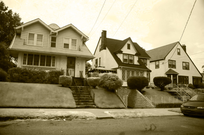 Three large houses with multiple stories sit high on sloping lawns.