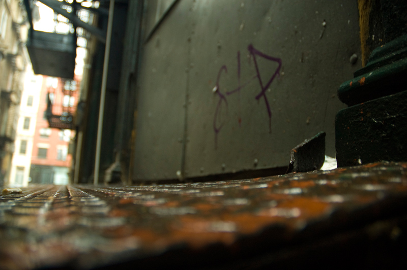 The metal platform of a loading dock is bent out of shape; there are fire escapes in the distance.